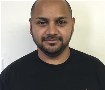 Bald male, with a beard and mustache smirking slightly with black shirt against a white backround